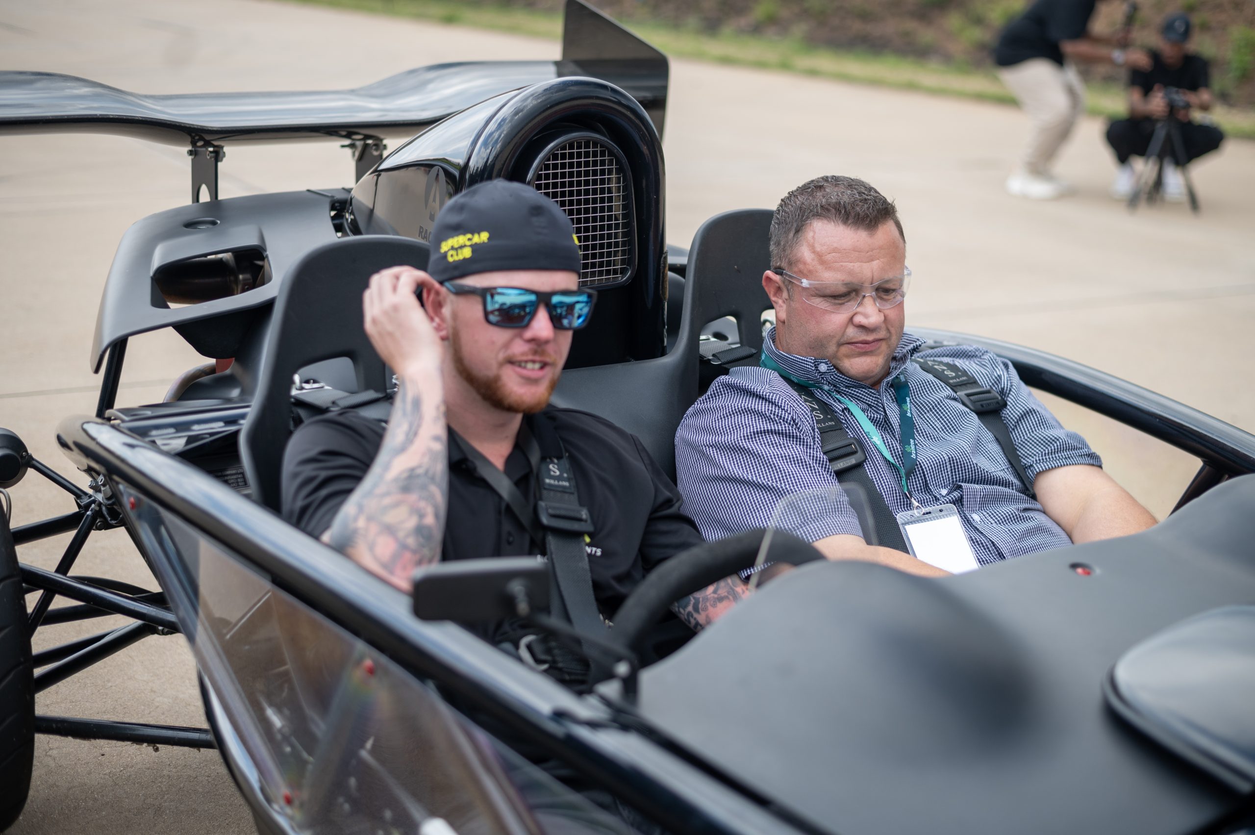 two people sitting in a small supercar without a roof