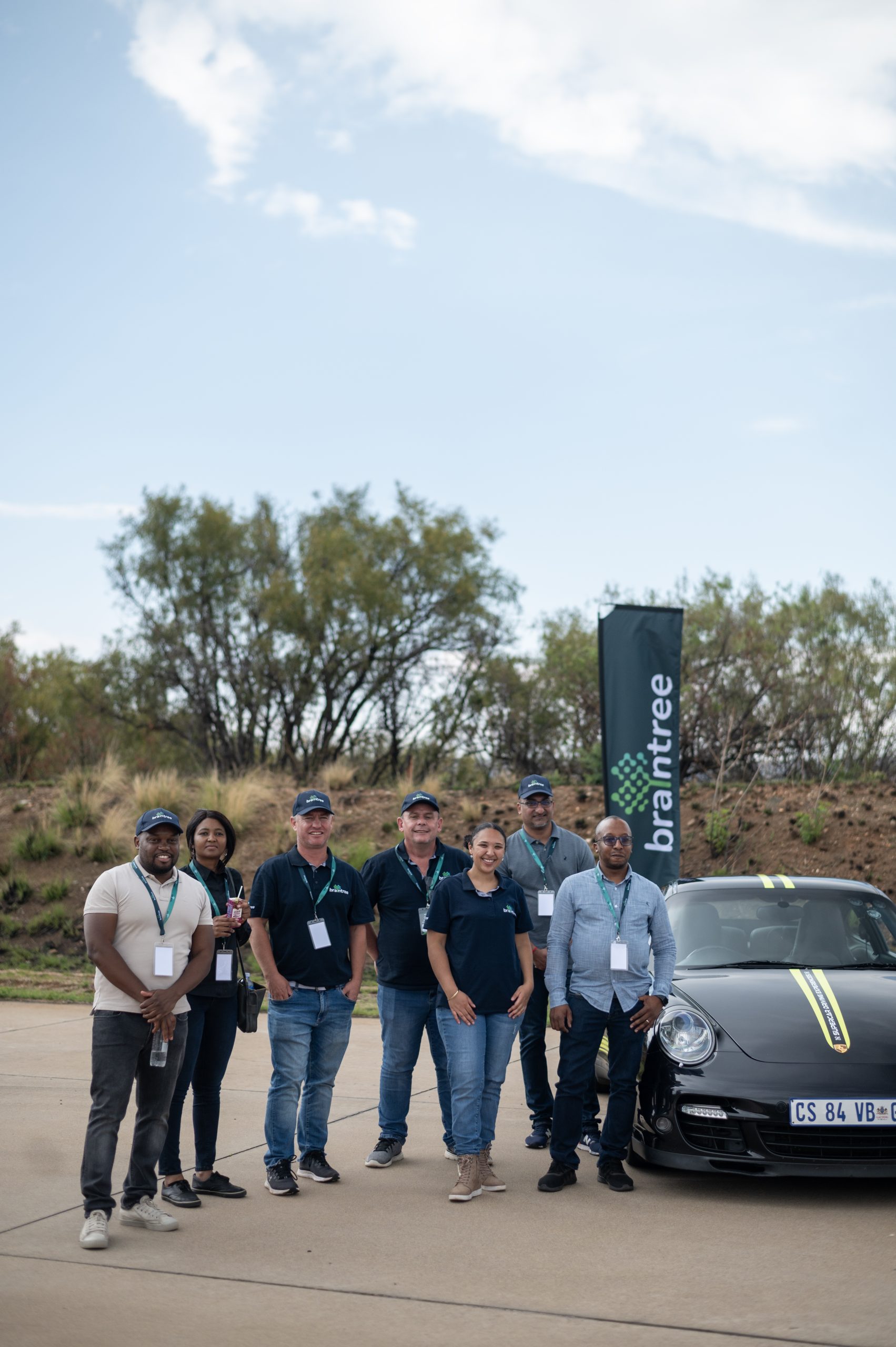 Braintree employees standing next to a black Porche