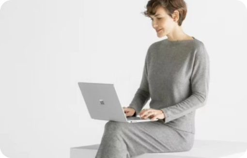 person sitting on a countertop while working on a Microsoft Surface Laptop 6